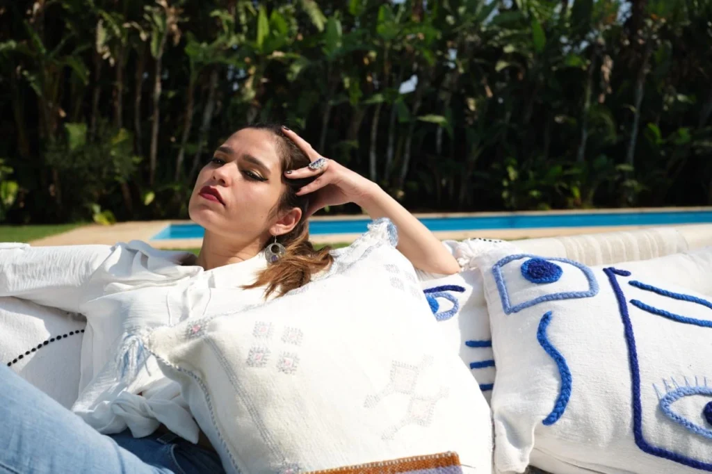 Femme assise sur un canapé avec les coussins Mazen, portant les bijoux de Mazen.